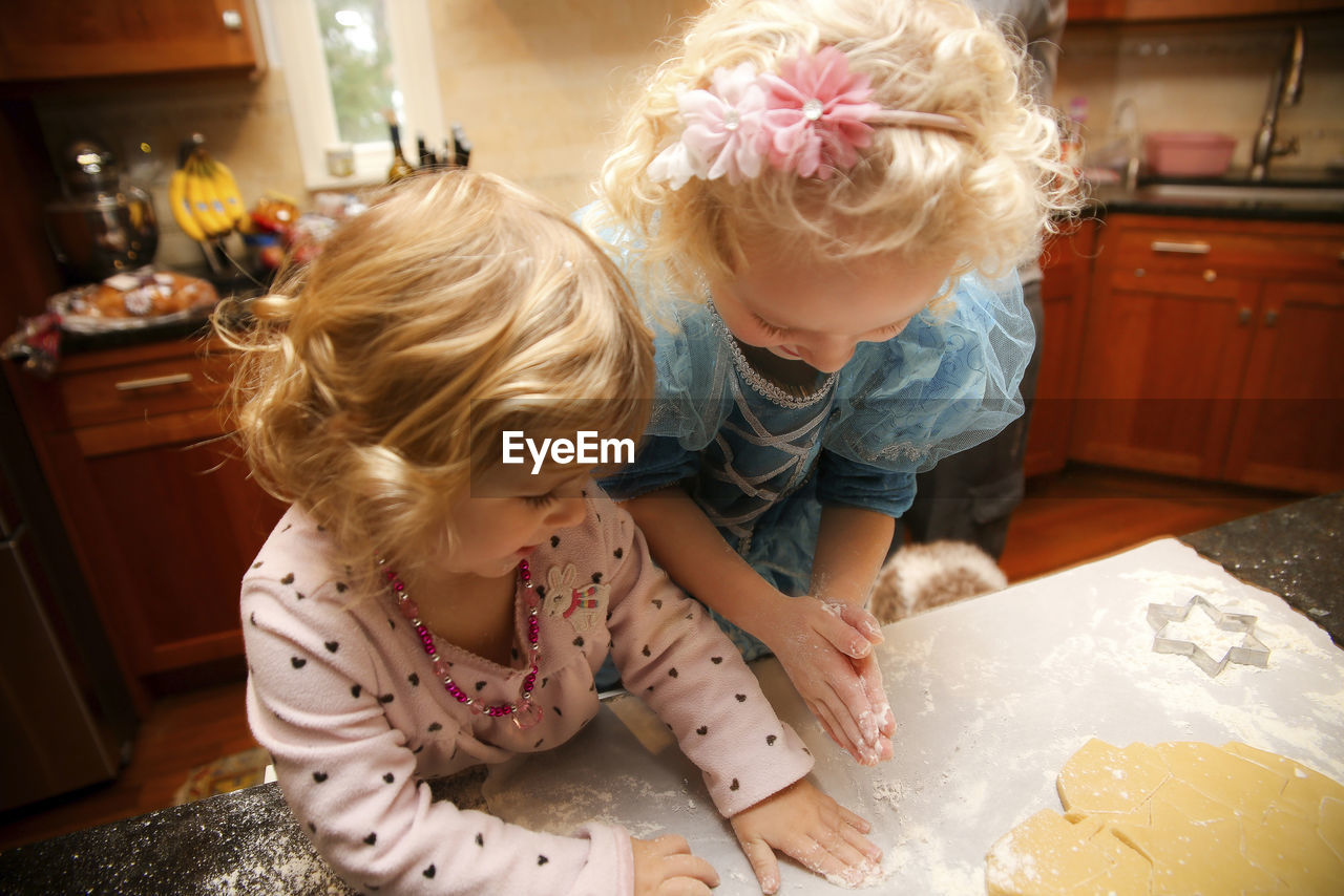 High angle view of happy sisters making cookies in kitchen at home