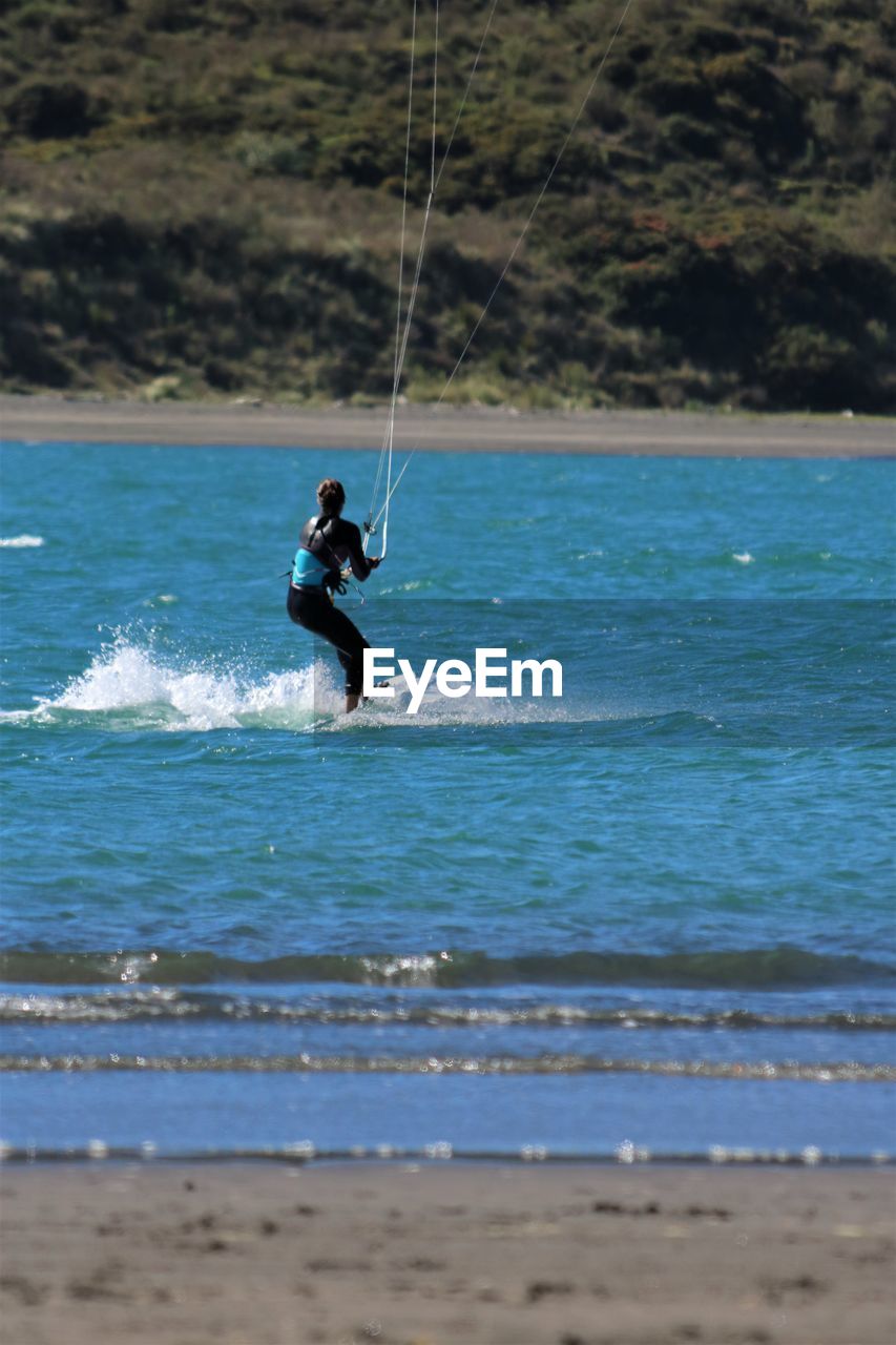 Side view of woman kiteboarding on sea during sunny day