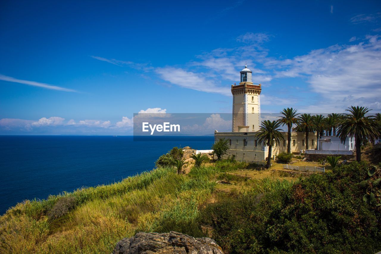 LIGHTHOUSE BY SEA AGAINST BUILDINGS