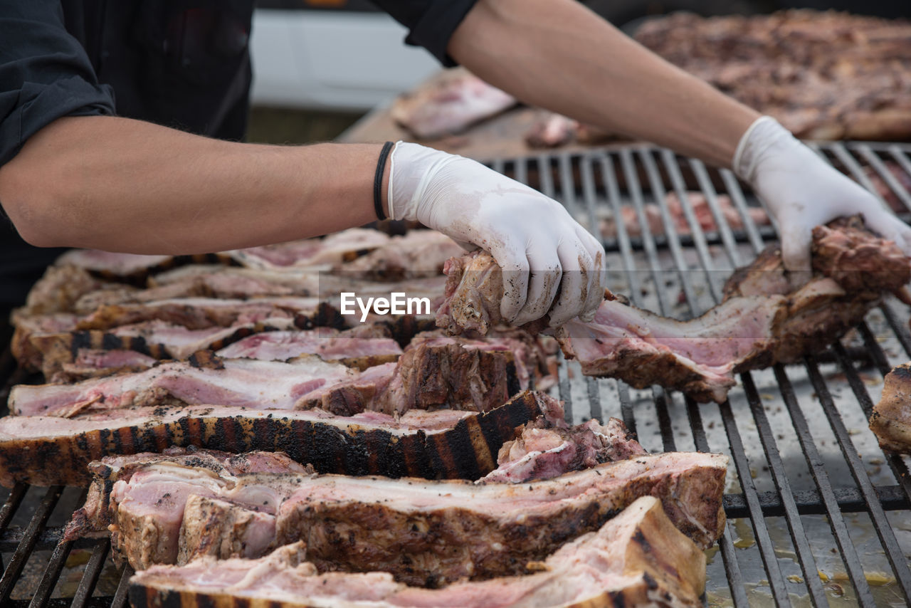 Midsection of person grilling pork on barbeque