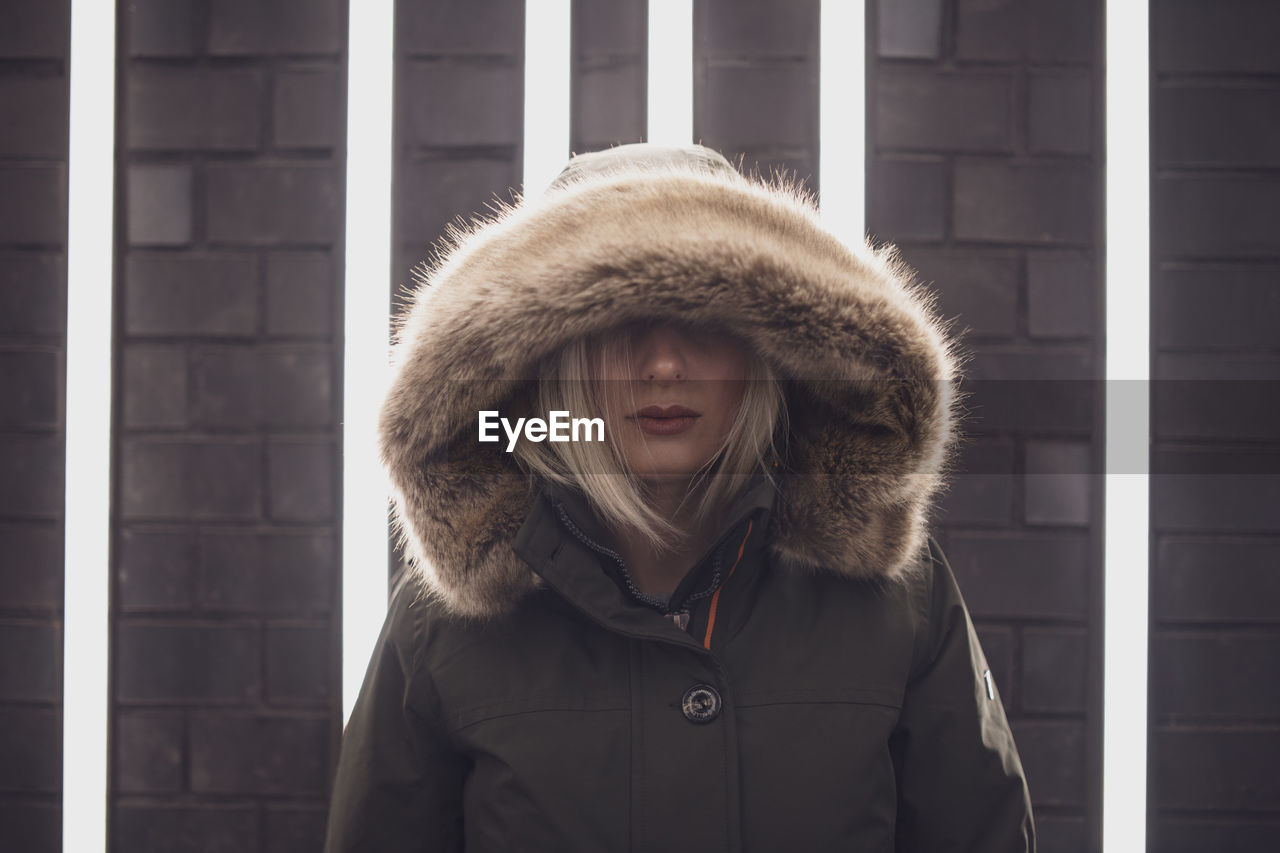 Close-up woman in hooded clothing standing against illuminated lights on wall