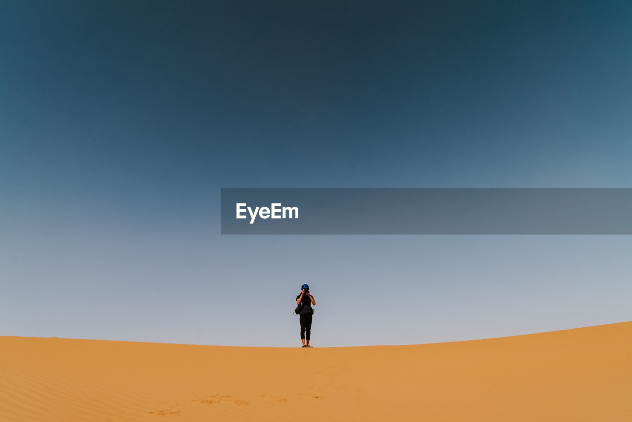 Man standing on sand dune in desert against clear sky