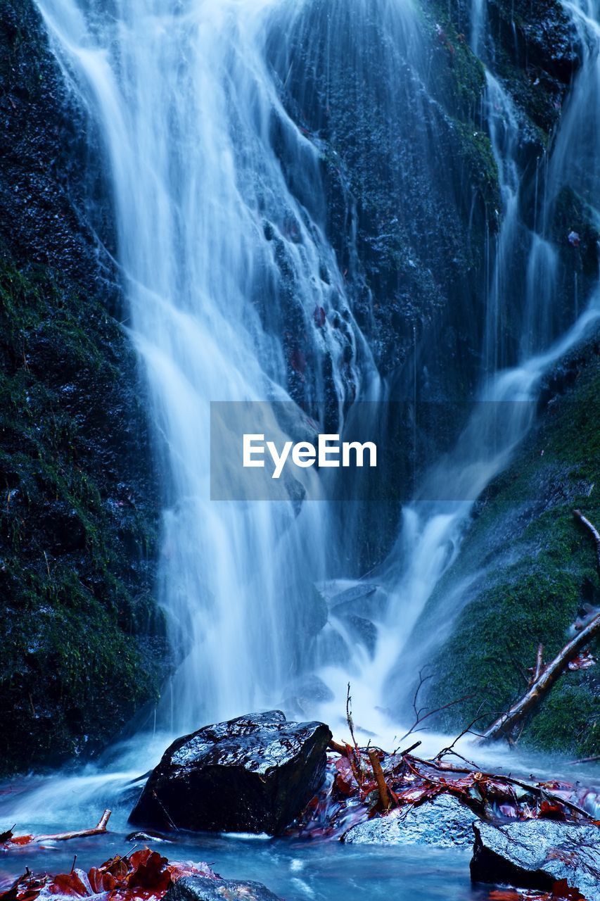 Water spray below small waterfall on mountain stream, water is falling over mossy boulder. the spray 