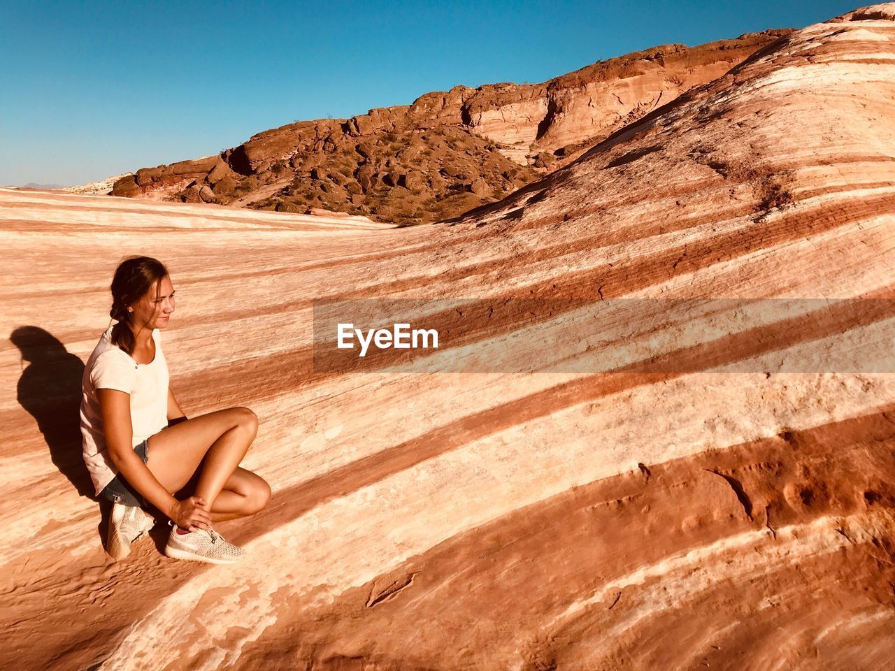 WOMAN SITTING ON SAND AT DESERT AGAINST SKY