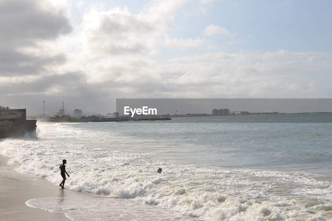 MAN SURFING ON SEA SHORE AGAINST SKY