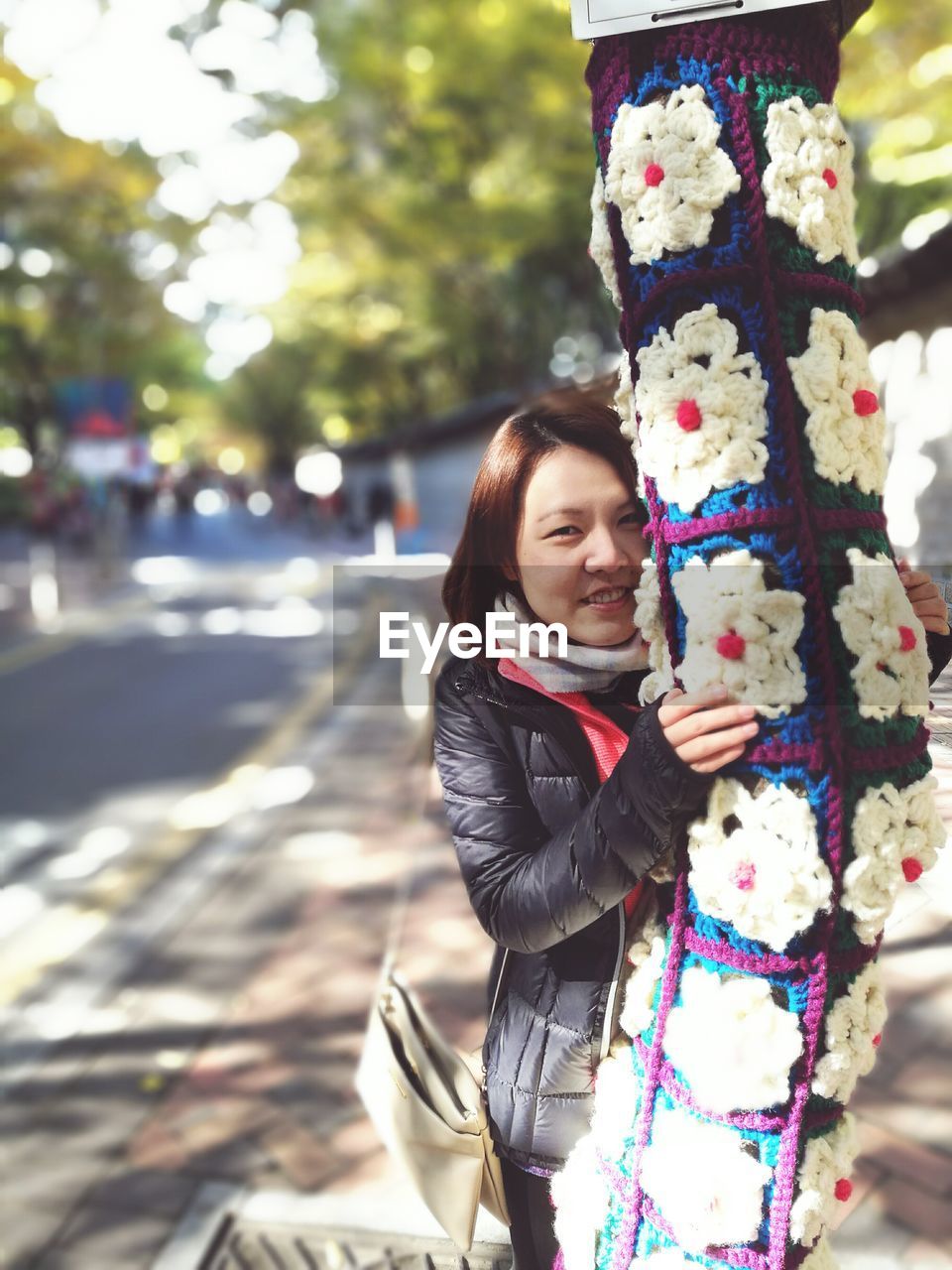 Portrait of young woman holding yarn bombing tree trunk at park