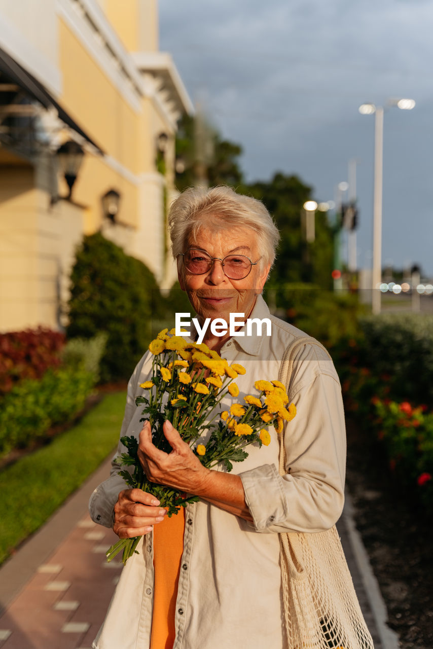 Portrait of smiling eldery women with yellow flowers  in orang dress