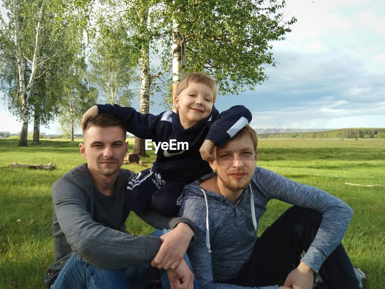 PORTRAIT OF HAPPY FATHER AND SON SITTING ON FIELD