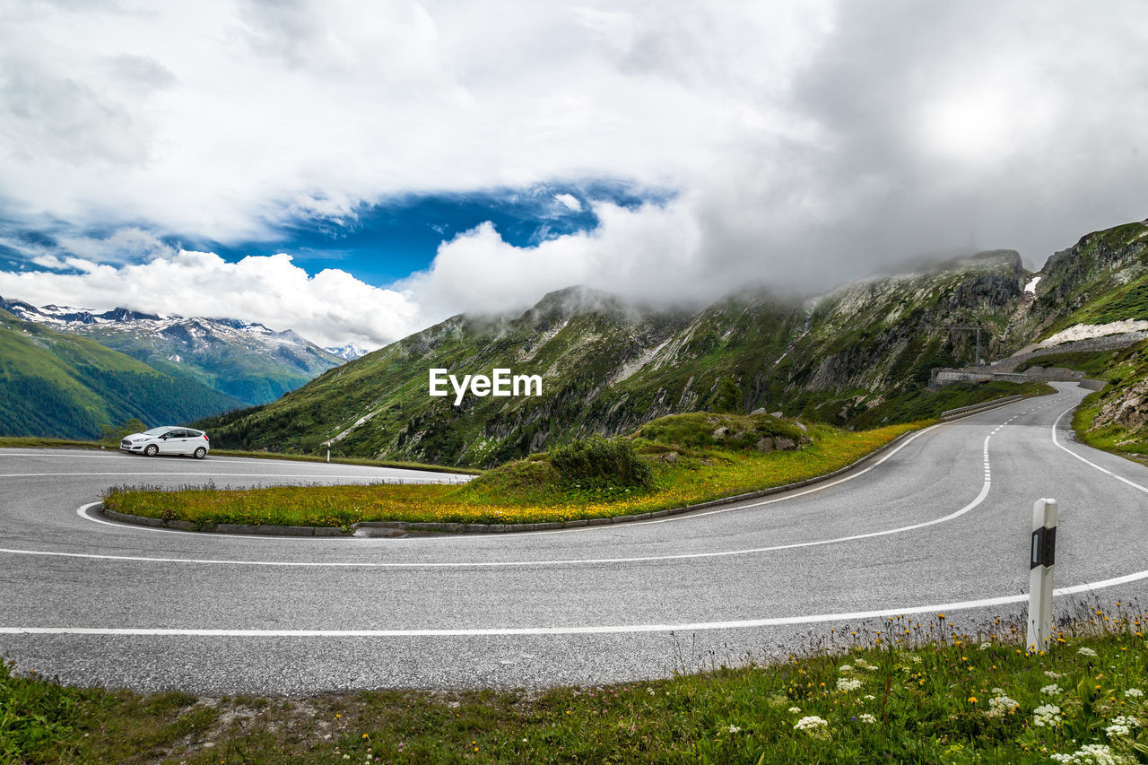 Road leading towards majestic mountains against cloudy sky