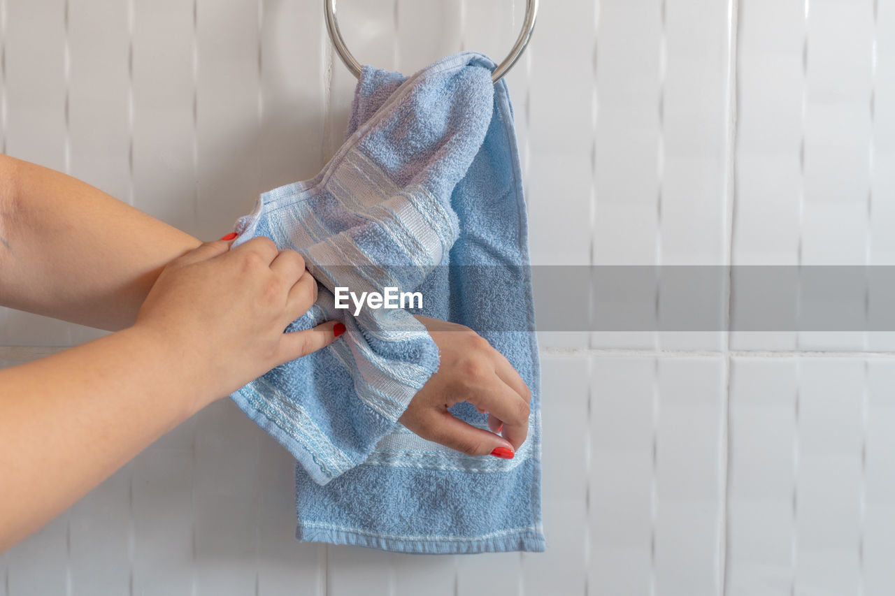 Cropped hands of woman cleaning with towel against wall