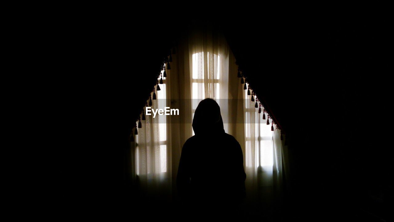 Silhouette person standing against curtain in darkroom