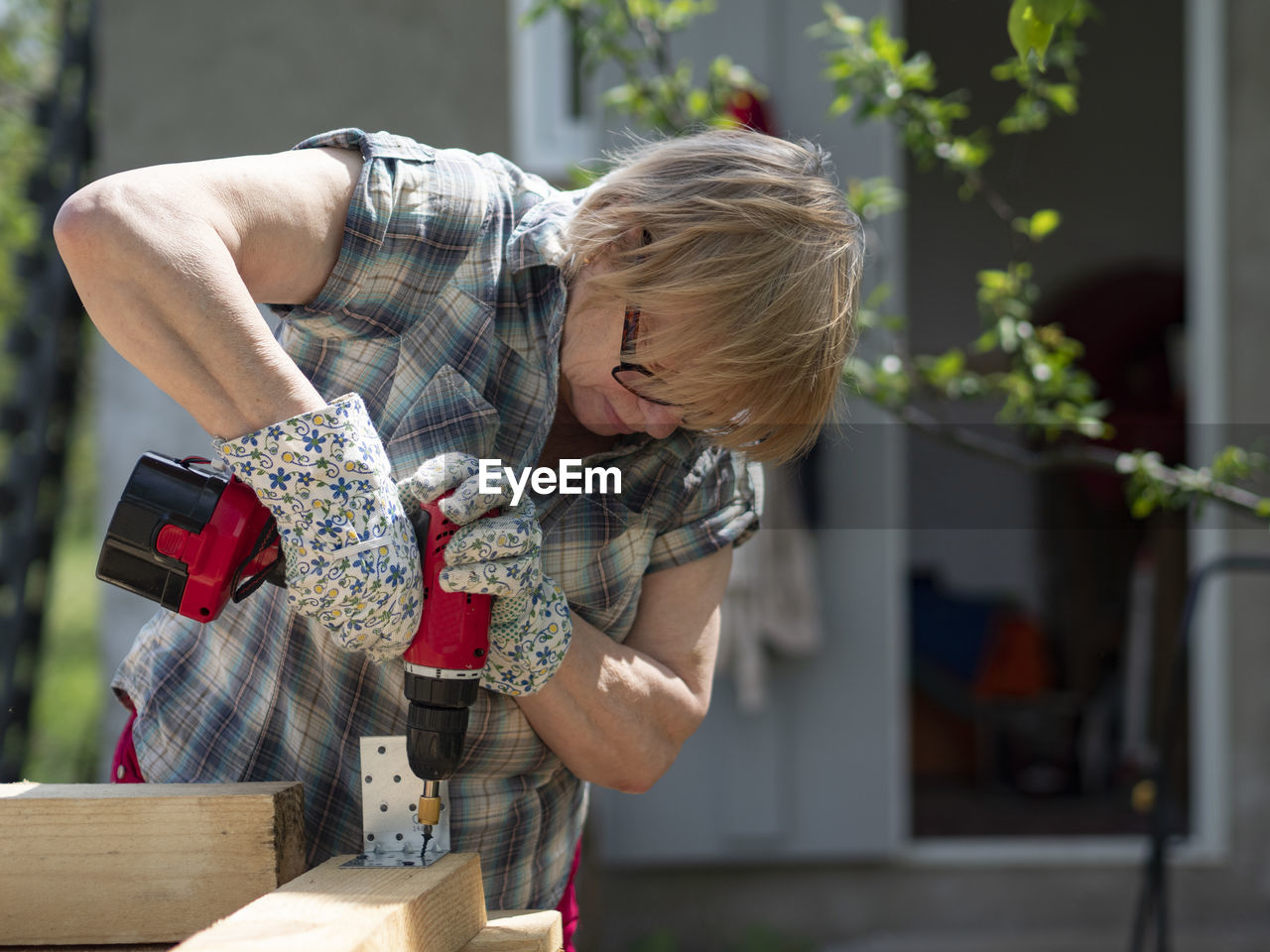 Senior caucasian woman assembles a wooden frame of building using metal fasteners using screwdriver