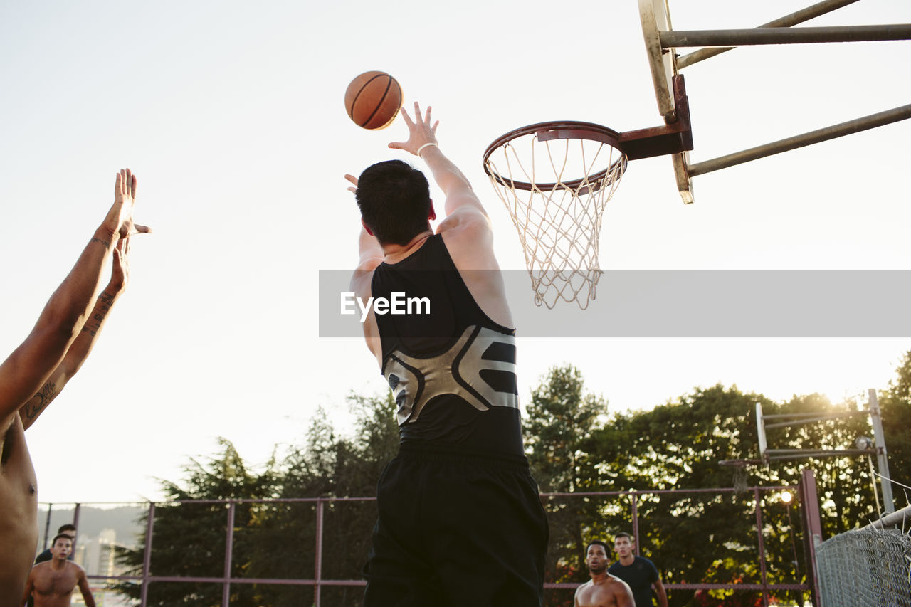 Man playing basketball with friends in court against clear sky