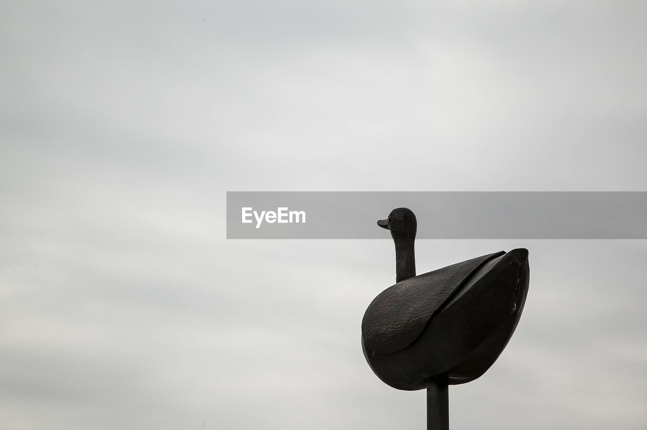 Low angle view of artificial bird against cloudy sky