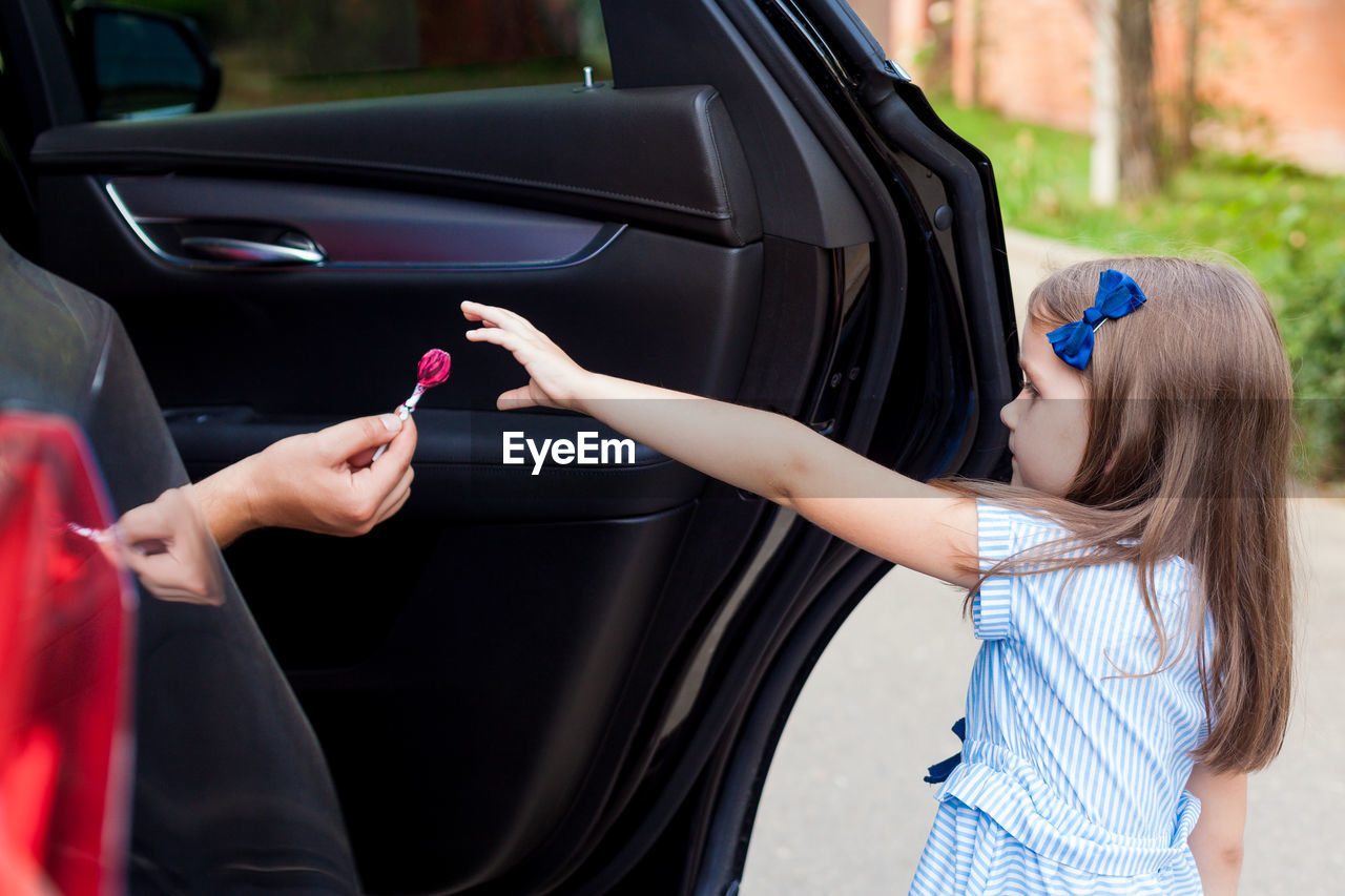 Cropped hand of person in car giving lollipop to girl on road