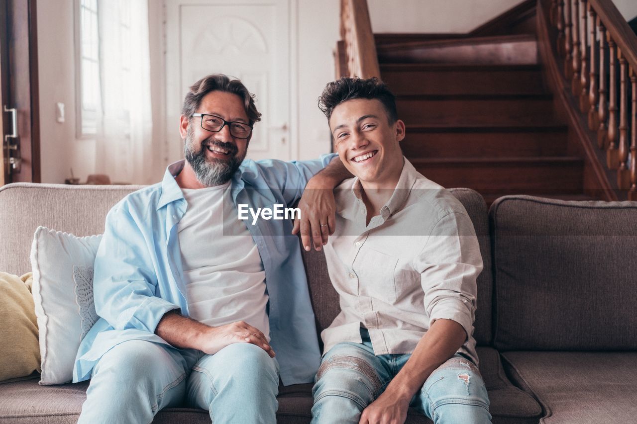 Portrait of smiling father and son sitting on sofa