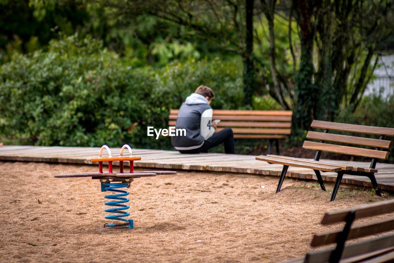 Spring ride with man in background sitting on boardwalk at playground