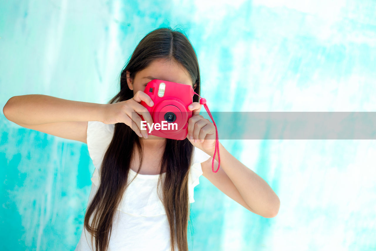 Teenage girl photographing with instant camera against wall