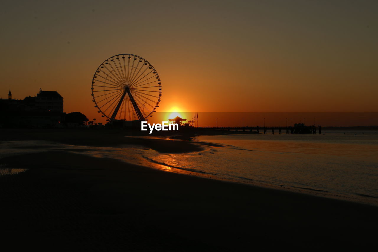 Ferris wheel at beach against sky during sunset