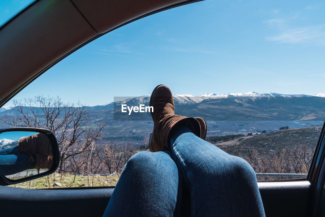 Female's feet sticking out of car window with a beautiful view of mountains under a clear sky