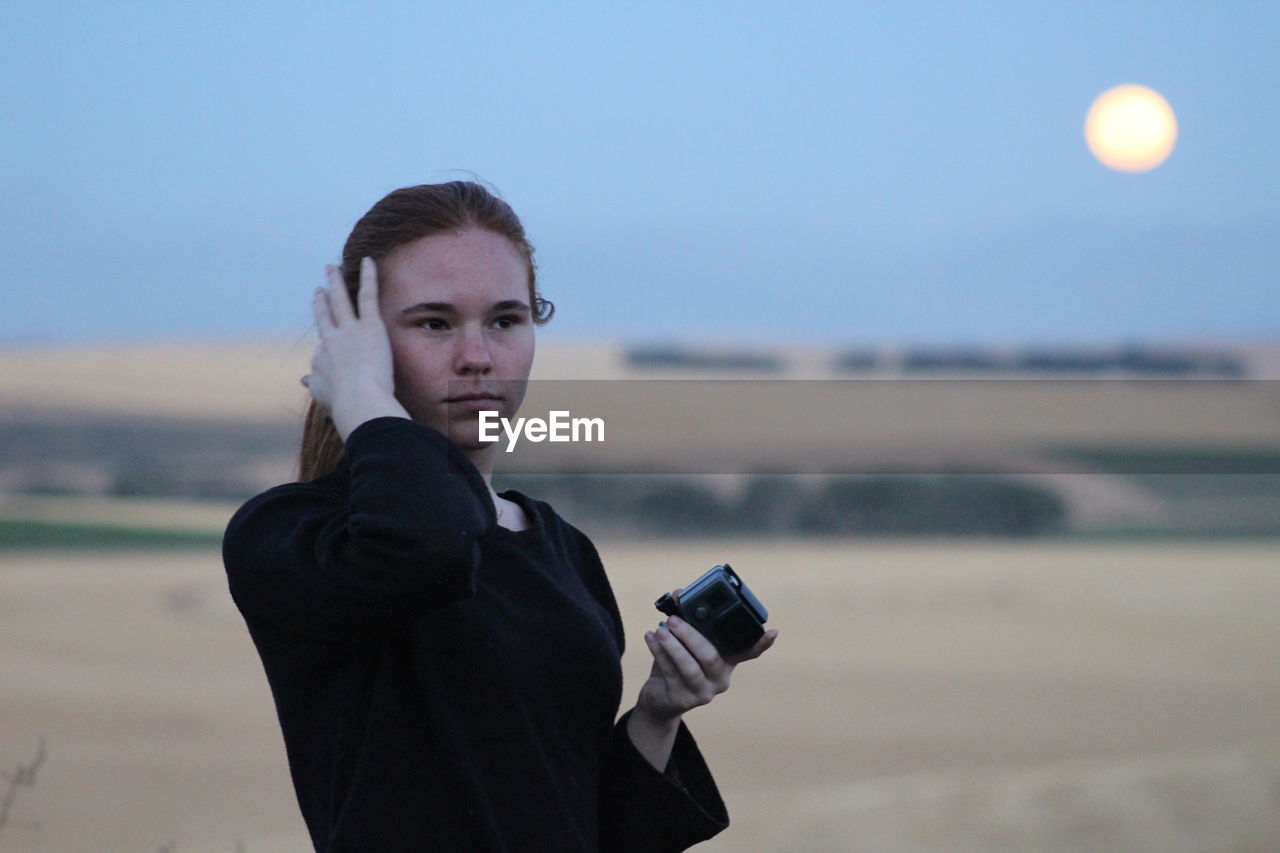 Woman looking away while holding camera at field