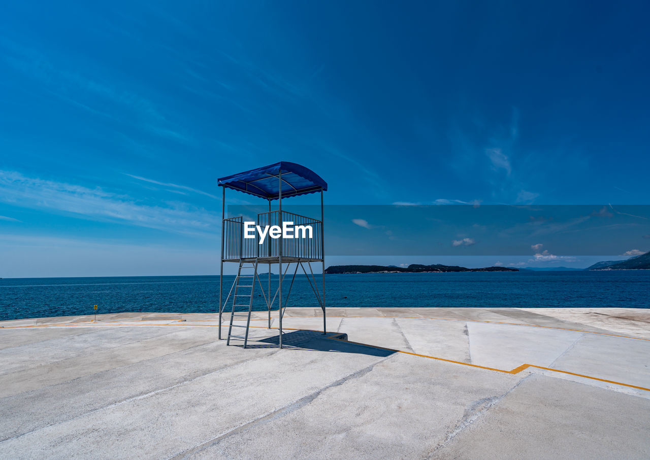 sky, ocean, water, sea, horizon, shore, coast, nature, beach, blue, land, scenics - nature, architecture, beauty in nature, horizon over water, lifeguard hut, tranquility, no people, cloud, tranquil scene, hut, outdoors, travel destinations, bay, lifeguard, security, day, built structure, protection, travel, summer, absence, trip, vacation, sand, man made structure, sunlight, sunny, observation point, pier, holiday, tower, idyllic