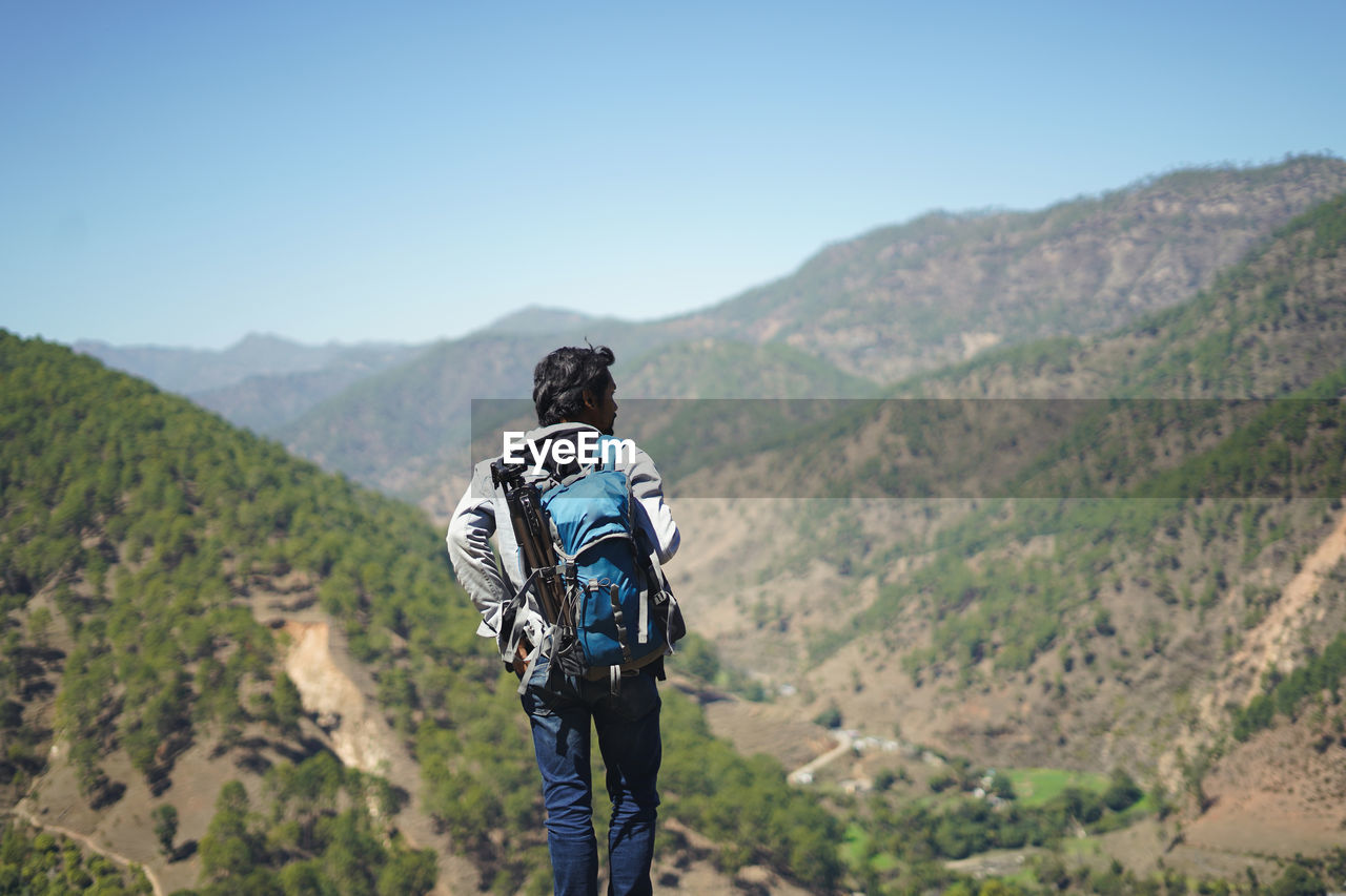 Young handsome indian boy standing on the top of the mountain with a bag pack , traveling