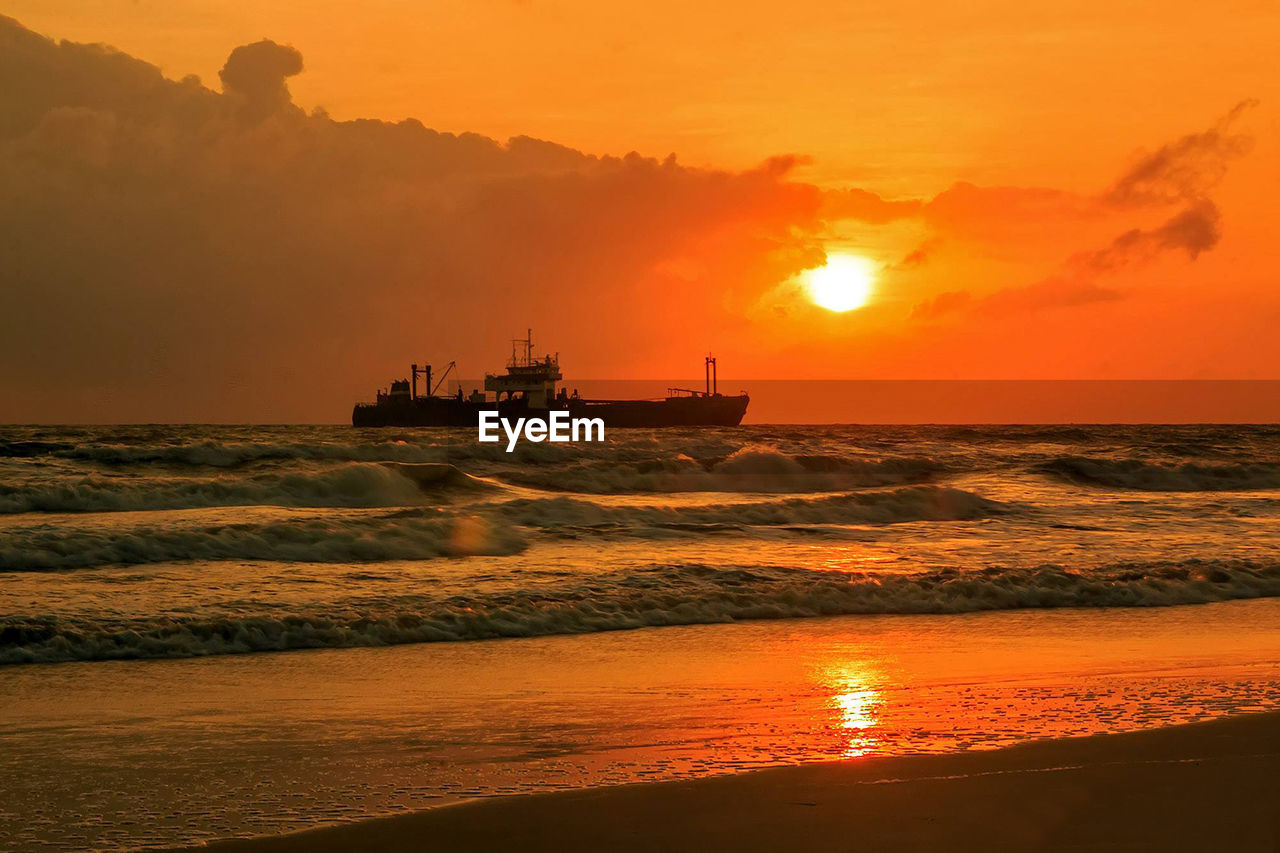 Cargo ship in sea against orange sky during sunset