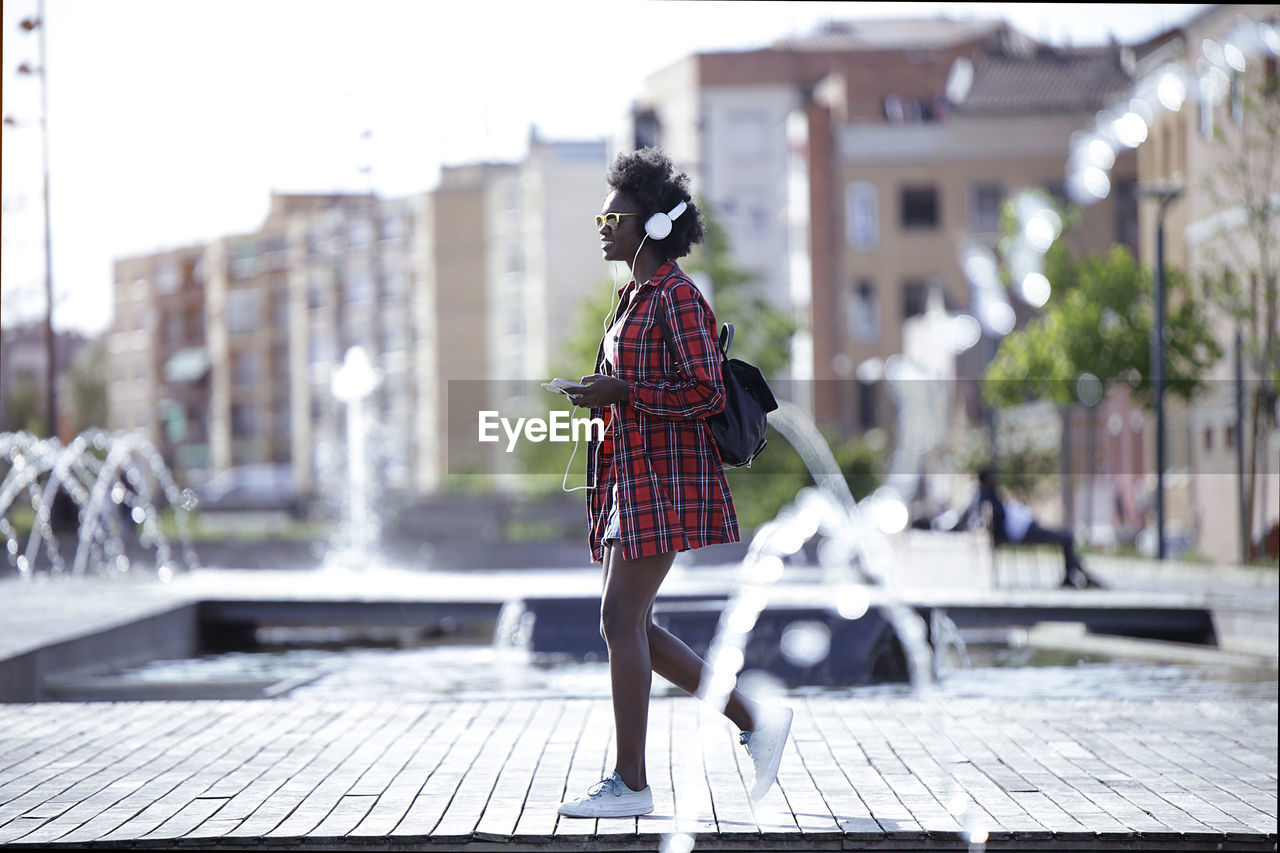 Young woman with backpack, smartphone and headphones walking in the city