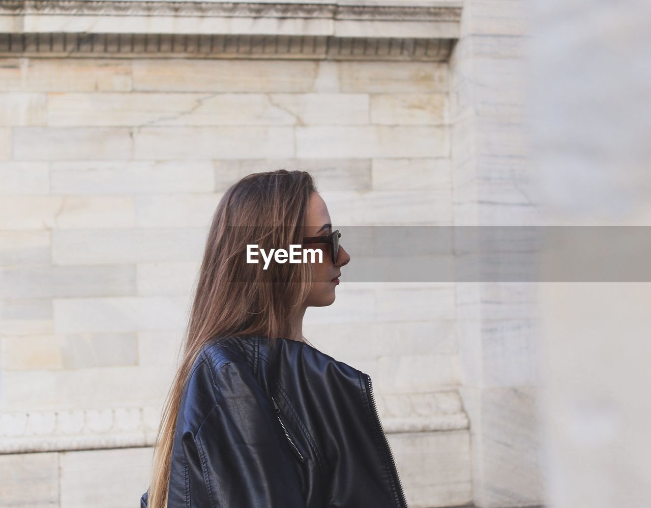 SIDE VIEW OF A YOUNG WOMAN LOOKING AWAY AGAINST WALL