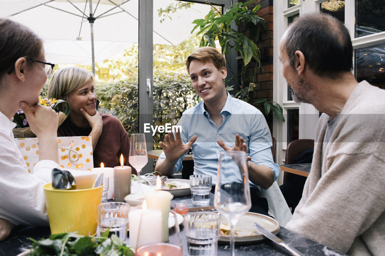 Smiling man gesturing and talking with family during party at restaurant