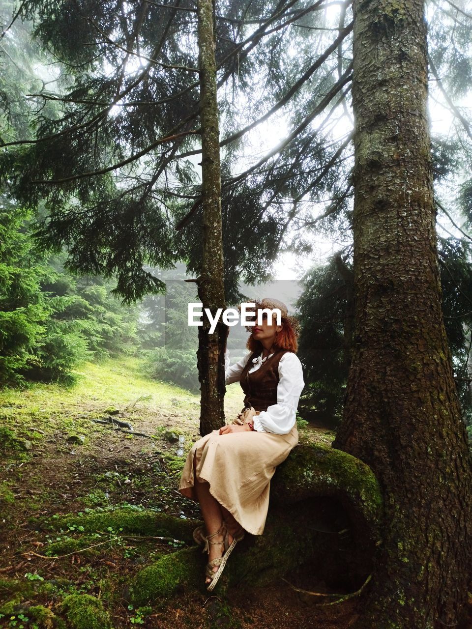 Woman by tree trunk in forest