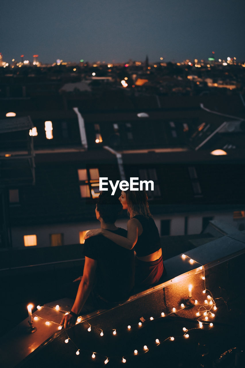 High angle view of couple sitting on illuminated terrace in city at dusk