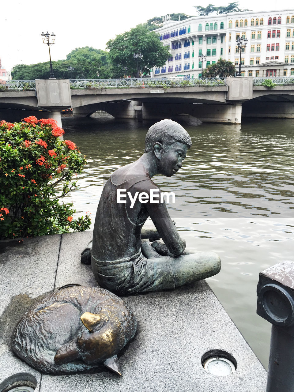 Bronze statue by river in city against clear sky