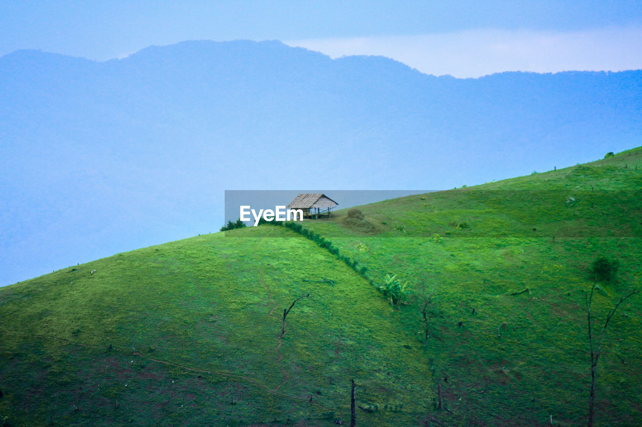 House on field by mountain against sky