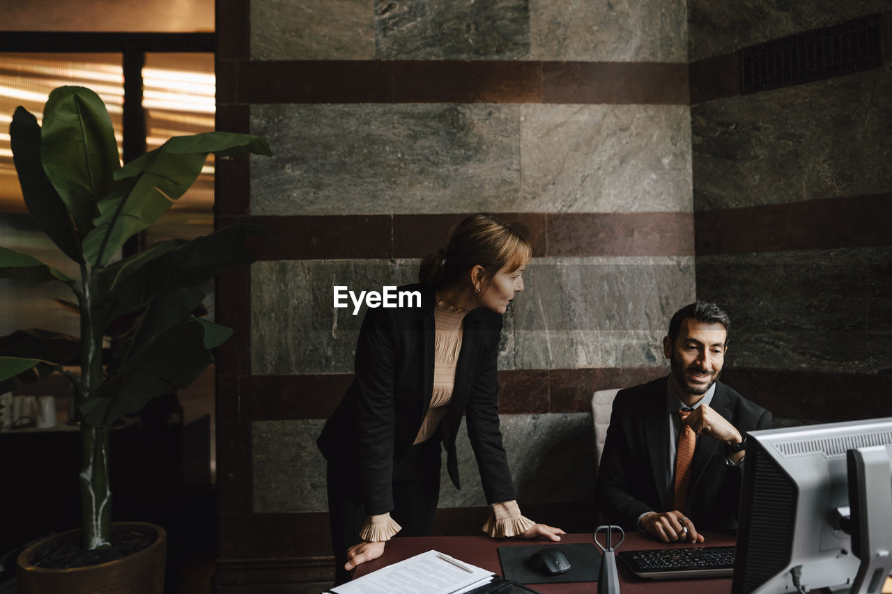 Businesswoman leaning on desk discussing with businessman at law office