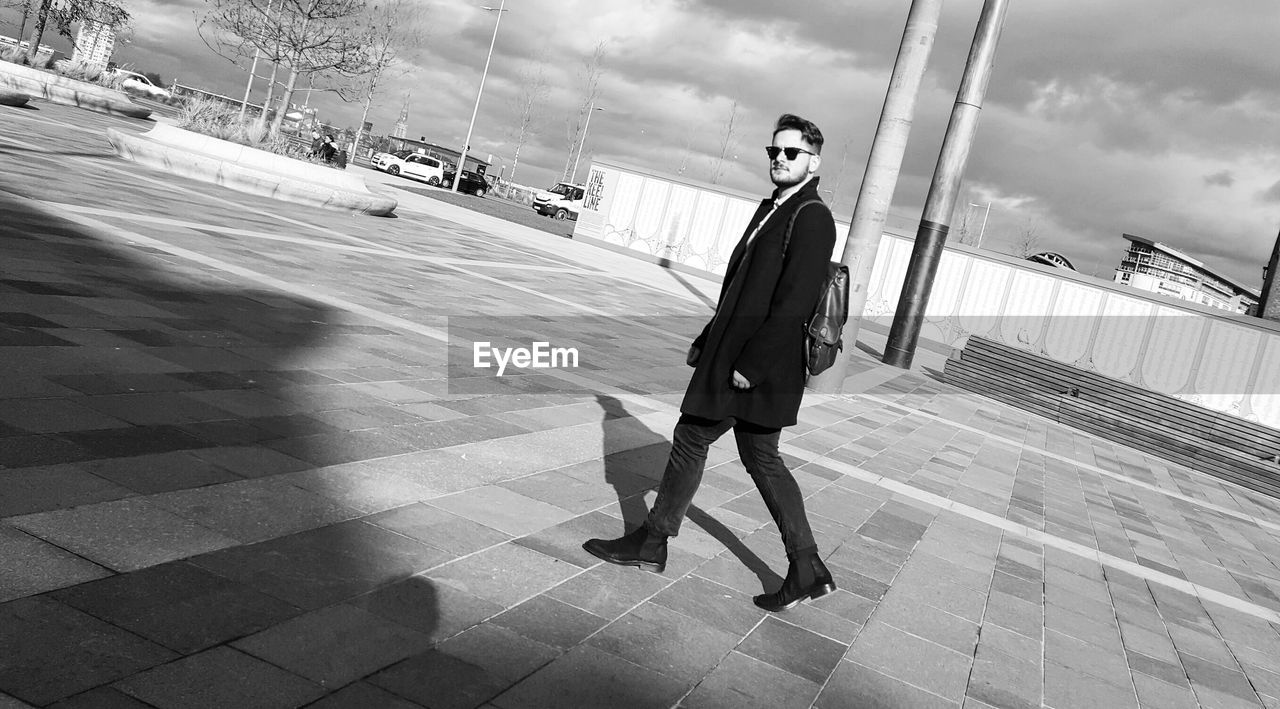 Tilt shot of stylish man walking on footpath against sky