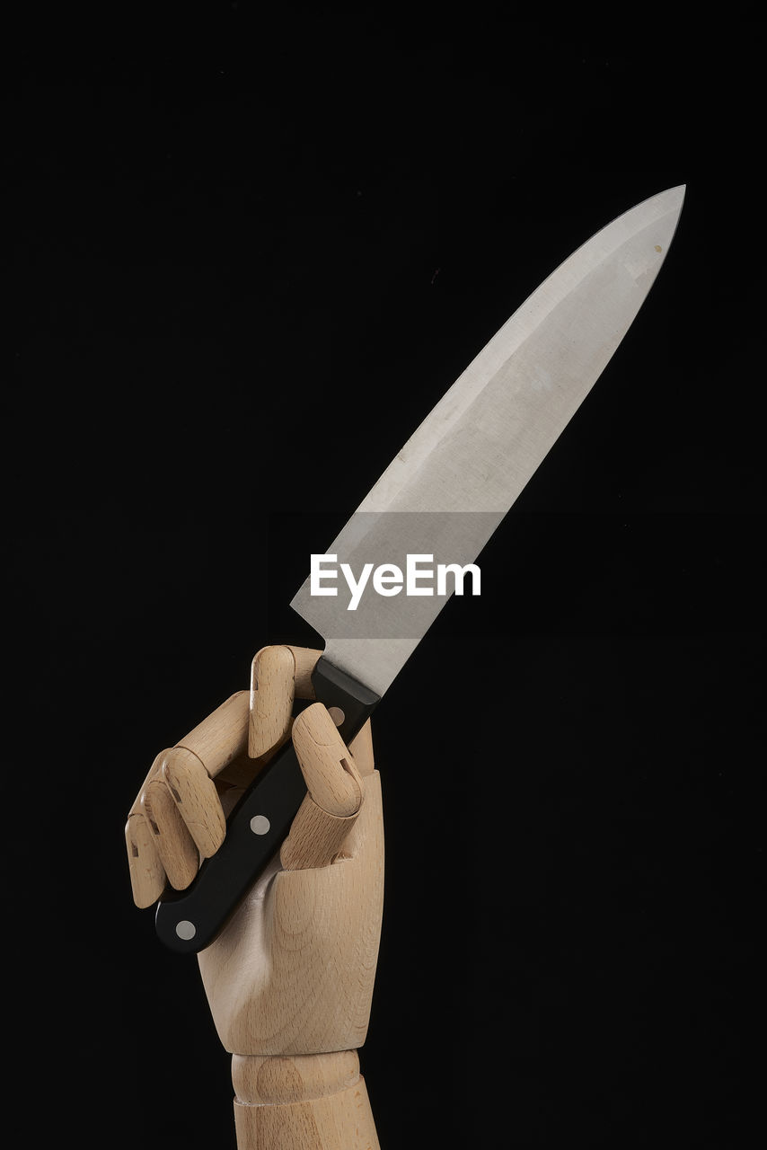 Sharp knife in wooden hand in studio on black background demonstrating concept of violence