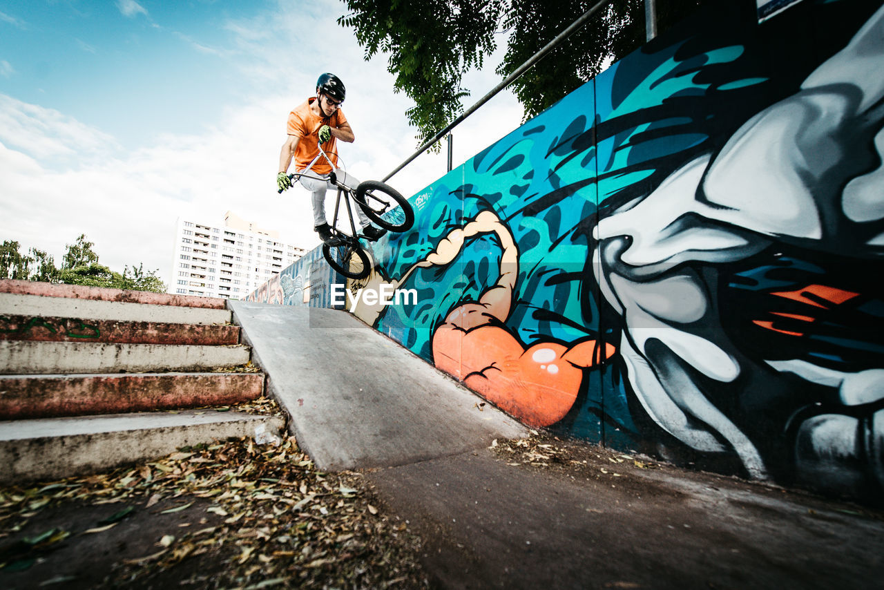 Man doing stunts with bicycle over steps by graffiti on wall