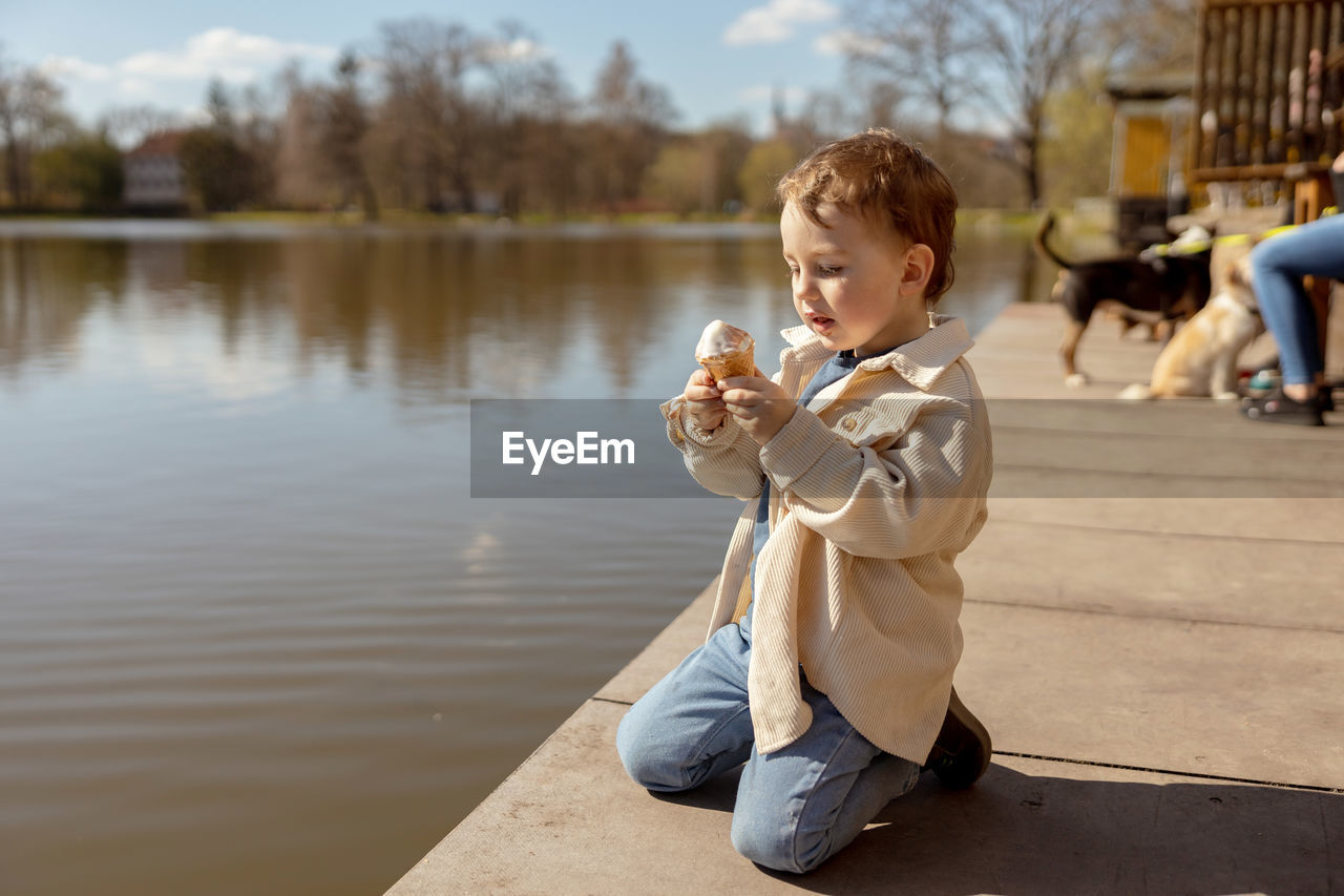 Little adorable boy sitting outdoors and eating ice cream. lake, water and sunny weather. 