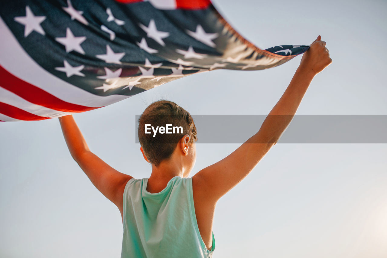 Rear view of boy holding american flag against clear sky