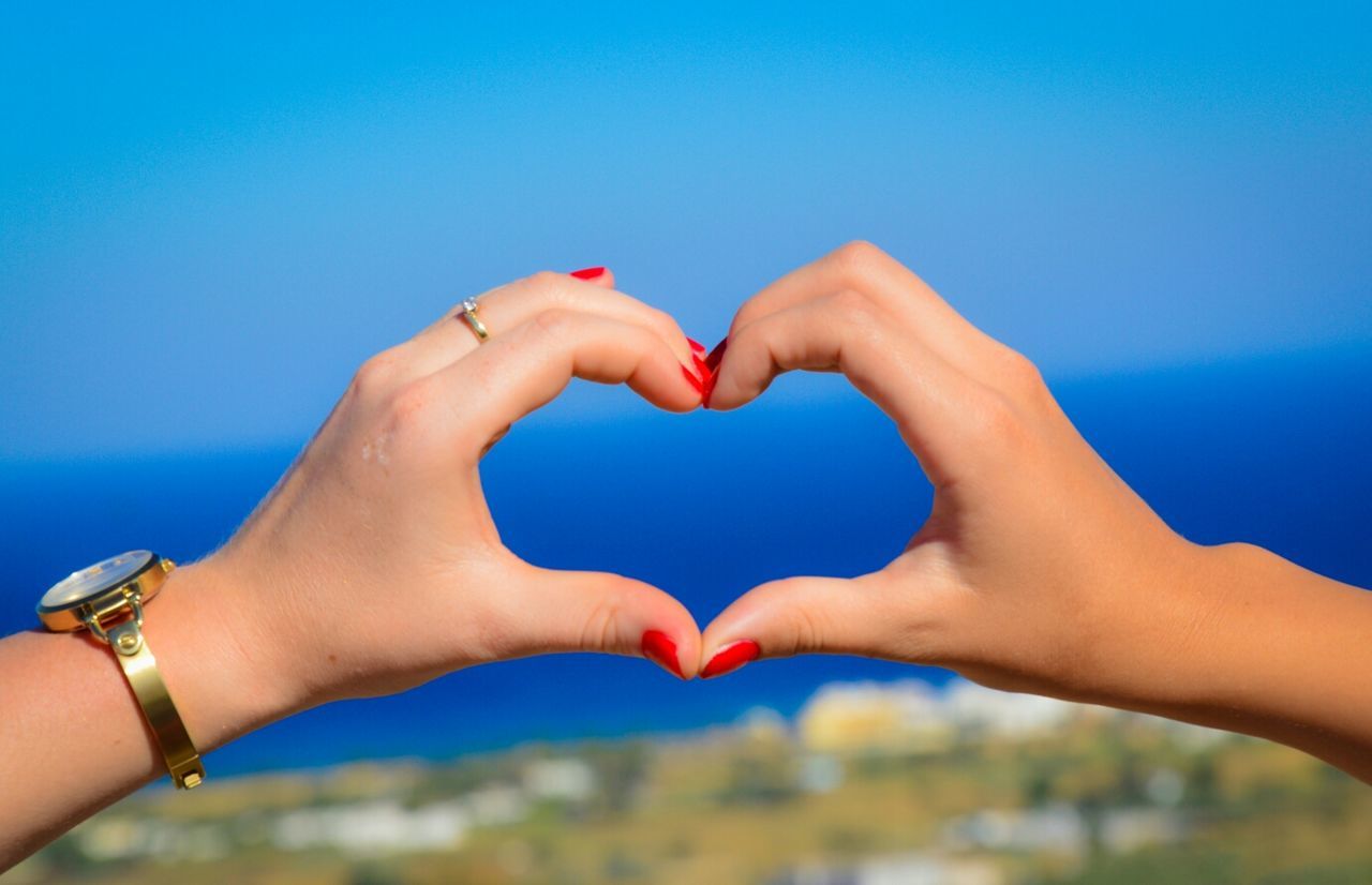 Close-up of hands making heart shape against blue sky