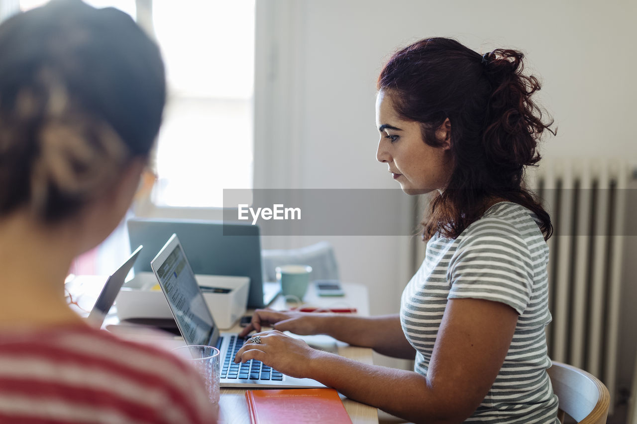 Focused ethnic woman typing on laptop working in office