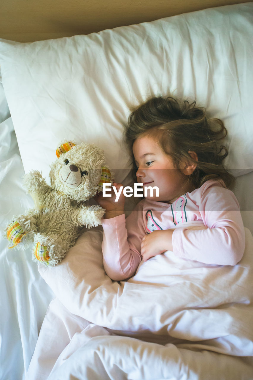 Girl lying on bed with stuffed toy at home