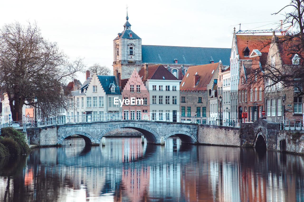 Arch bridge over river by buildings in city against sky