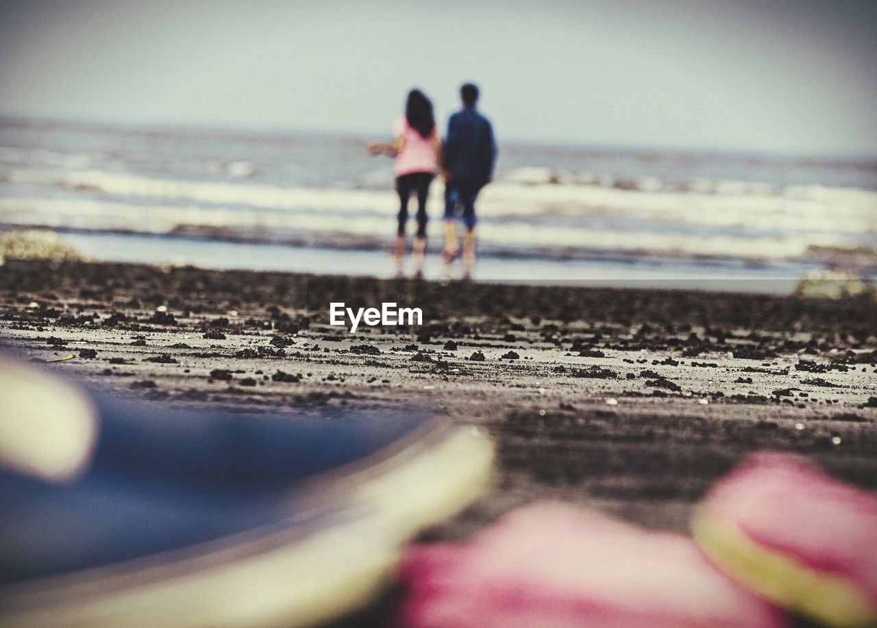 Rear view of couple walking at beach against sky