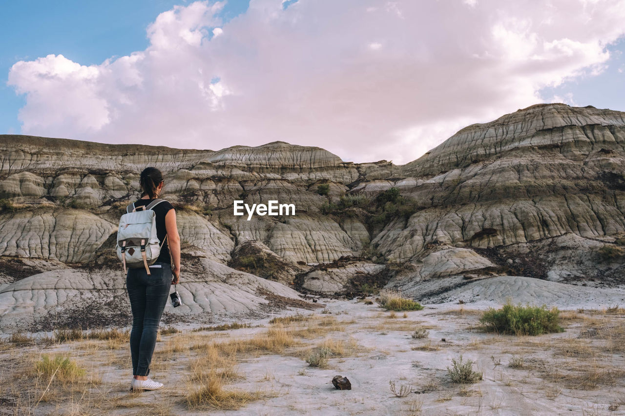 REAR VIEW OF WOMAN STANDING ON MOUNTAIN AGAINST SKY