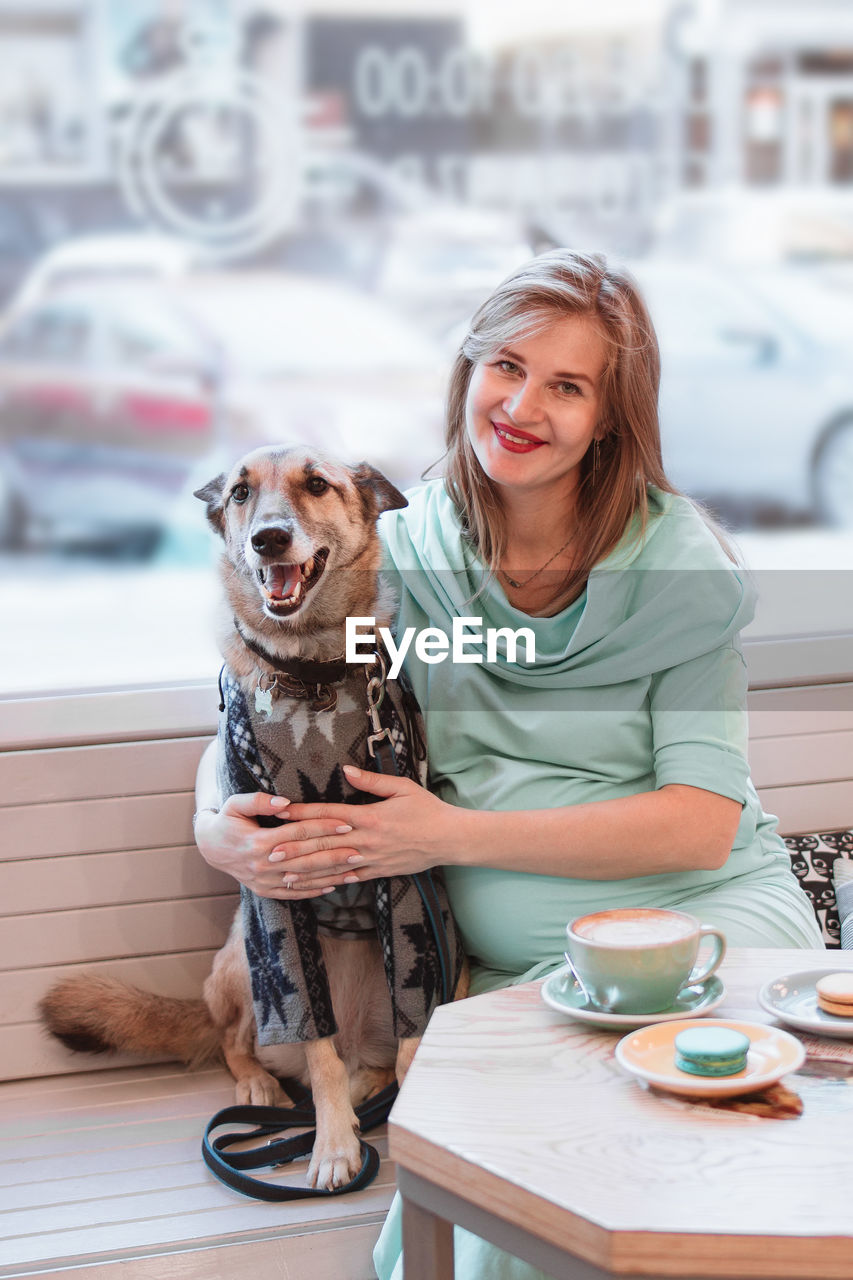 Portrait of smiling pregnant caucasian women with her dog in cafe. pregnant lifestyle.