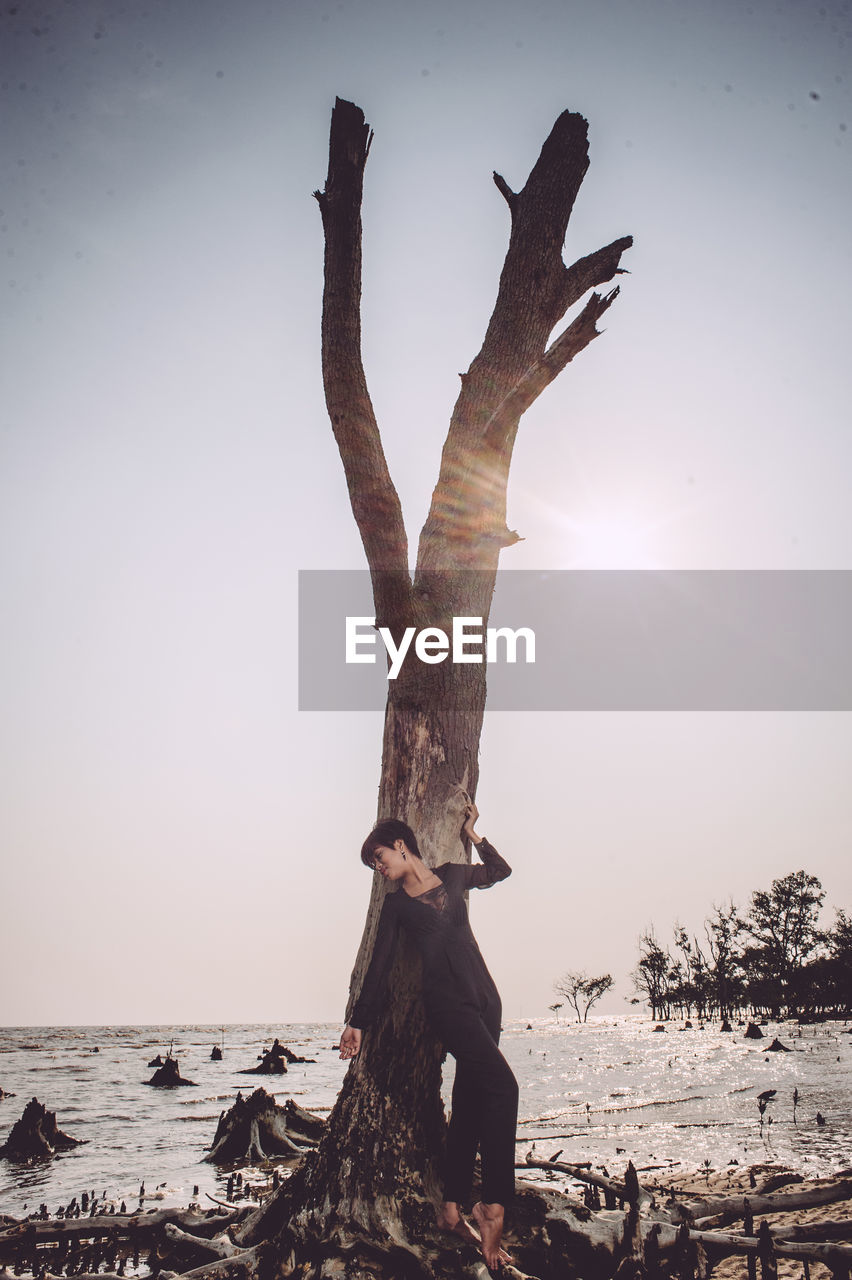 Woman standing against driftwood at beach against sky