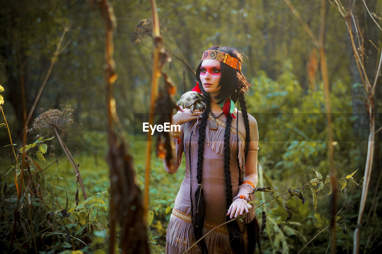 Young woman in traditional clothing carrying tortoise in forest